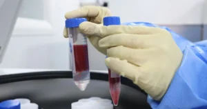 Mãos com luvas segurando tubos de sangue sobre uma centrífuga