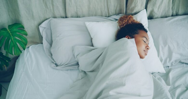 Mulher dormindo em uma cama de lençóis brancos