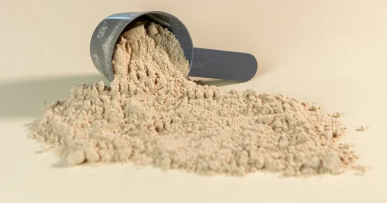 Scoop de whey protein em pó derramado sobre um fundo bege